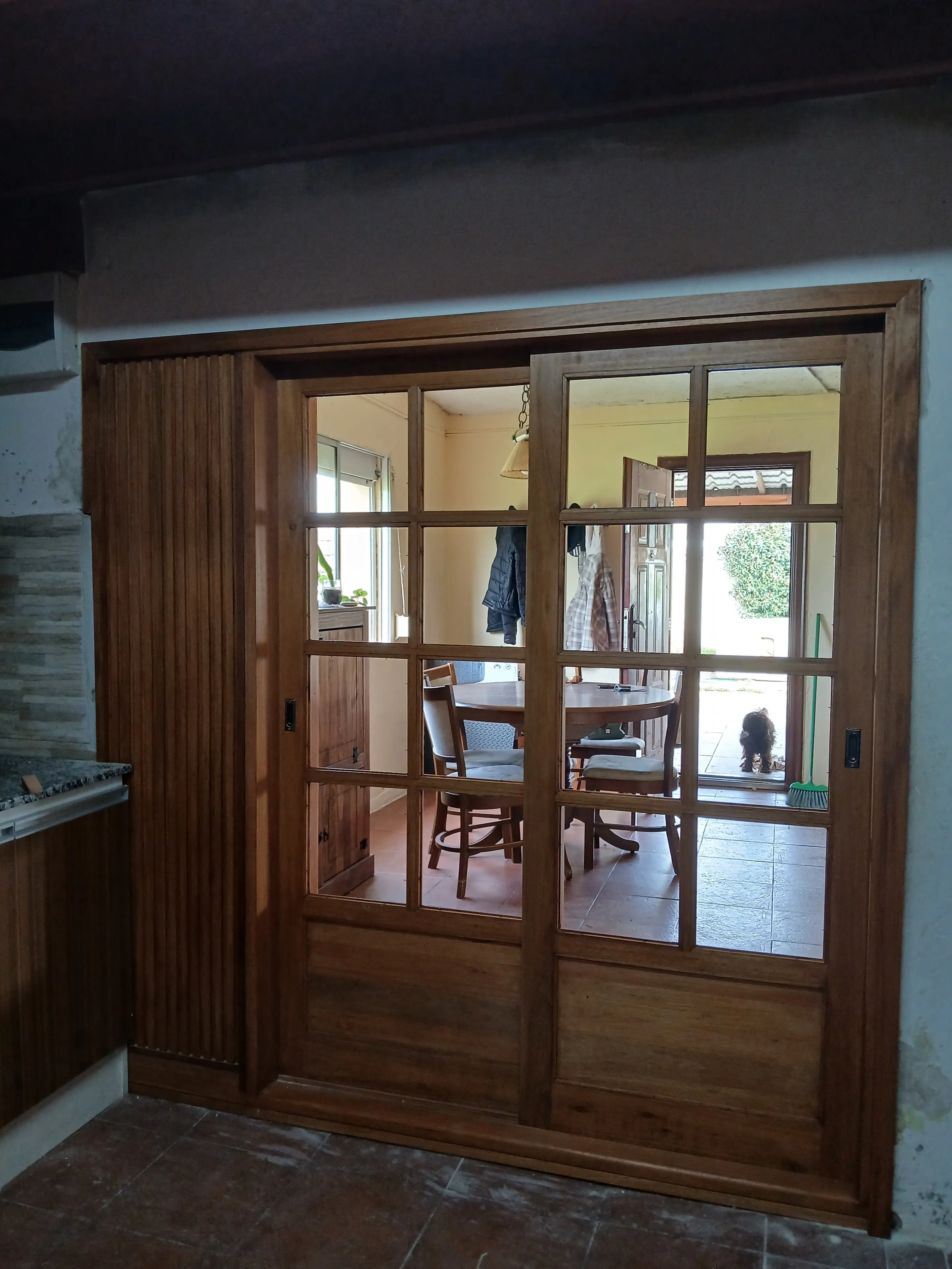 Puerta corrediza doble de madera maciza, vidriada a cuarterones, con banderola y postigón plegable al costado
