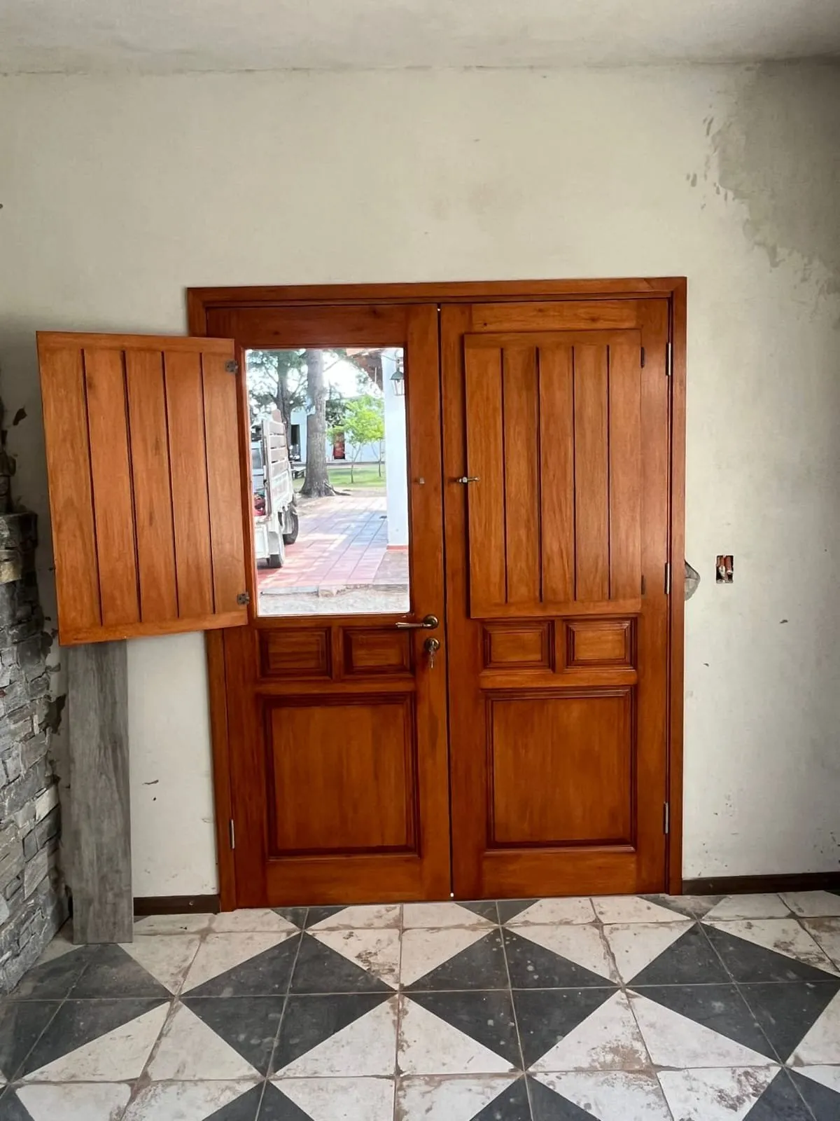 Puerta de entrada doble de madera maciza, con postigón abierto sobre la hoja vidriada