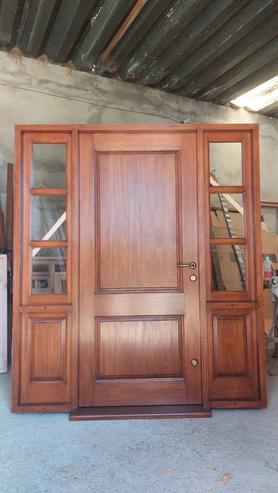Puerta de entrada de madera maciza con dos paños laterales vidriados, terminada en el taller