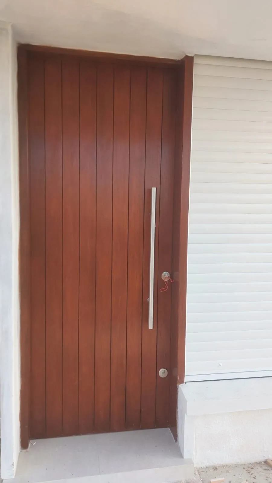 Puerta exterior de tablas verticales de madera con tirador largo de acero, ya colocada