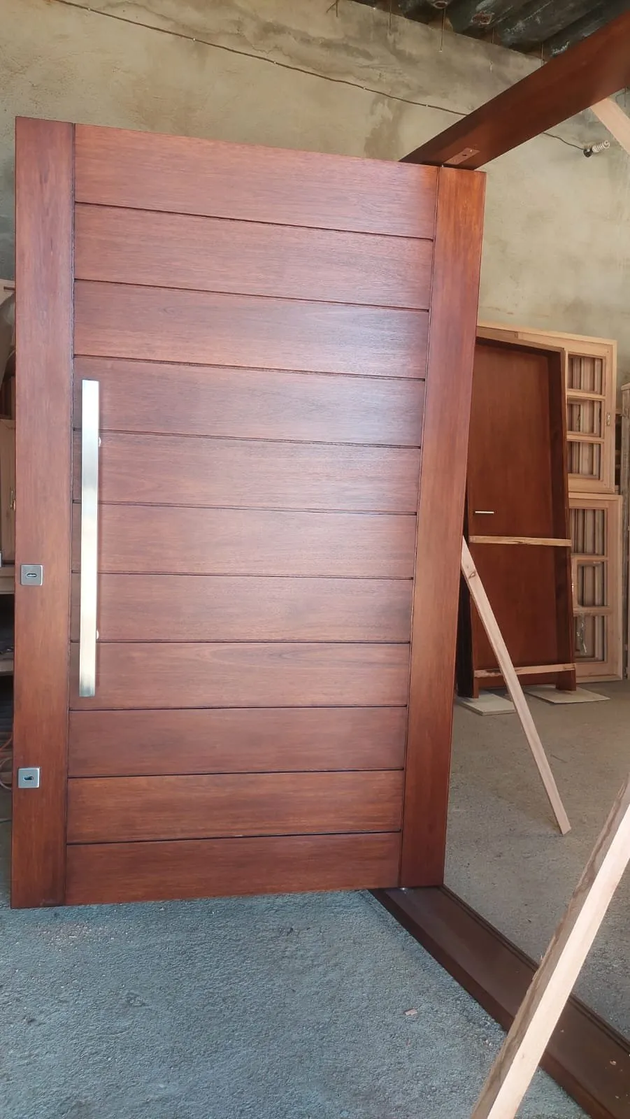 Puerta pivotante de madera rojiza con tablas horizontales y tirador largo de acero, en el taller