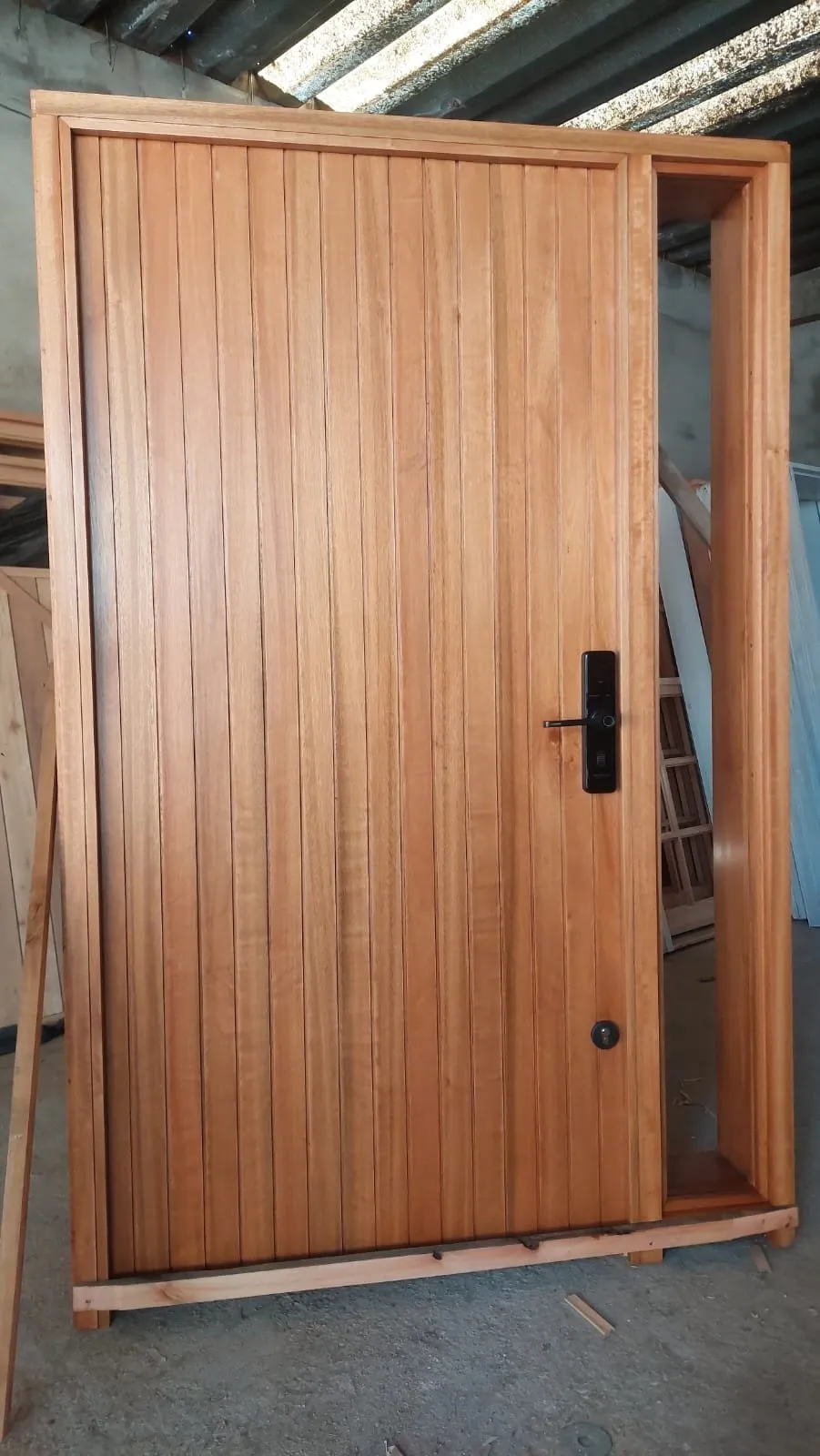 Puerta de madera clara de tablas verticales con cerradura digital y paño lateral, en el taller